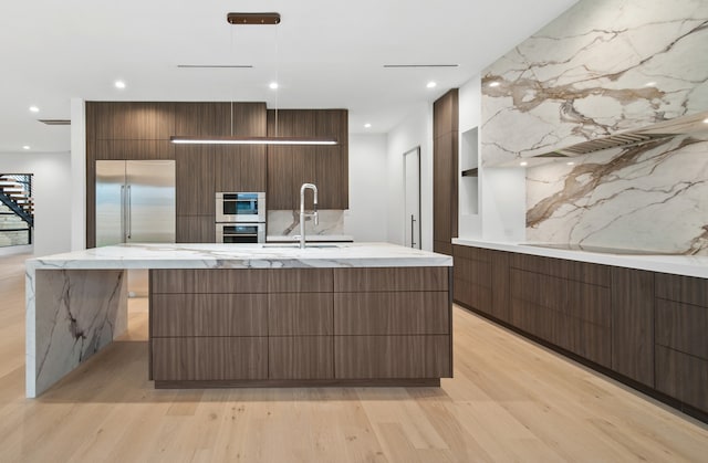 kitchen featuring a large island with sink, appliances with stainless steel finishes, sink, and light wood-type flooring