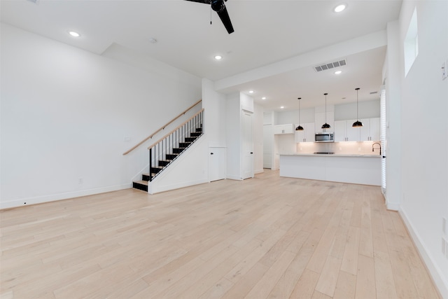 unfurnished living room with light hardwood / wood-style floors, sink, and ceiling fan