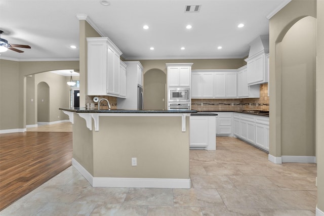 kitchen with a kitchen breakfast bar, backsplash, ornamental molding, stainless steel appliances, and light hardwood / wood-style flooring