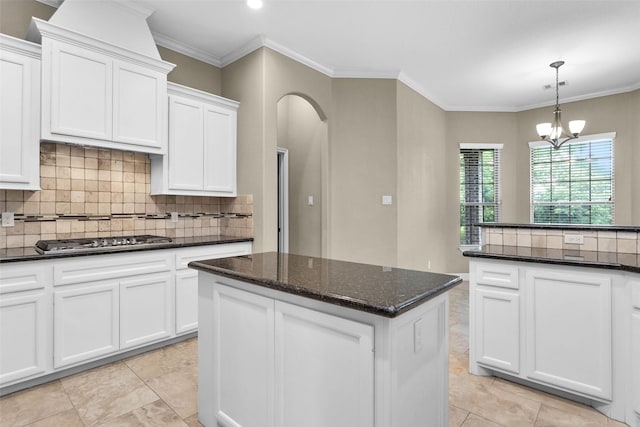 kitchen with white cabinetry, dark stone countertops, crown molding, a chandelier, and decorative light fixtures