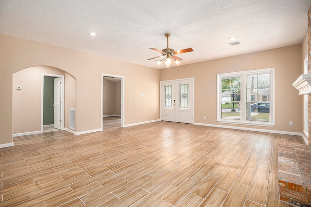 unfurnished living room with light hardwood / wood-style floors, a textured ceiling, and a brick fireplace