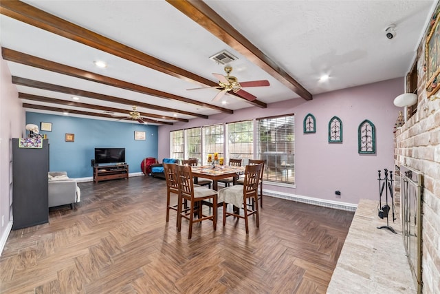 dining area with beam ceiling, dark parquet flooring, ceiling fan, a brick fireplace, and a textured ceiling