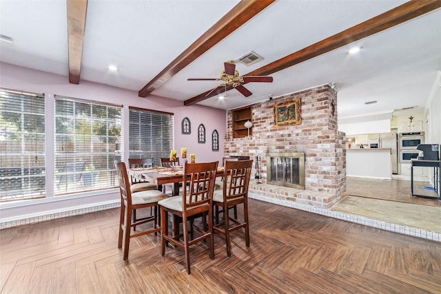 dining room featuring beamed ceiling, ceiling fan, dark parquet floors, and a brick fireplace