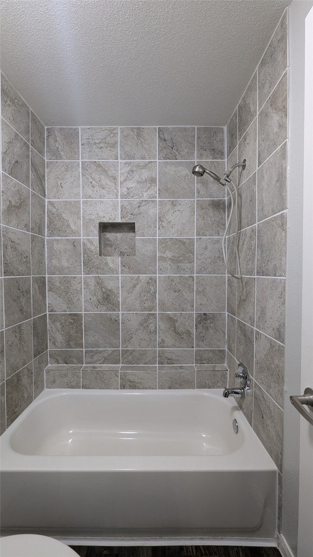 bathroom with tiled shower / bath combo, a textured ceiling, and toilet