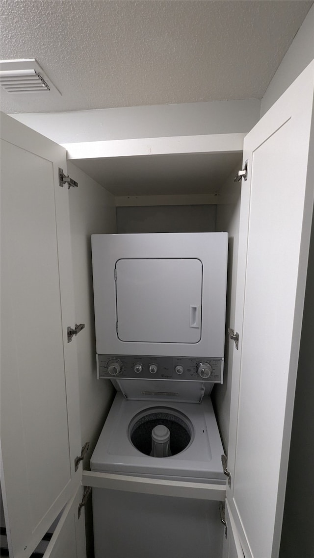 laundry area featuring stacked washer / drying machine and a textured ceiling