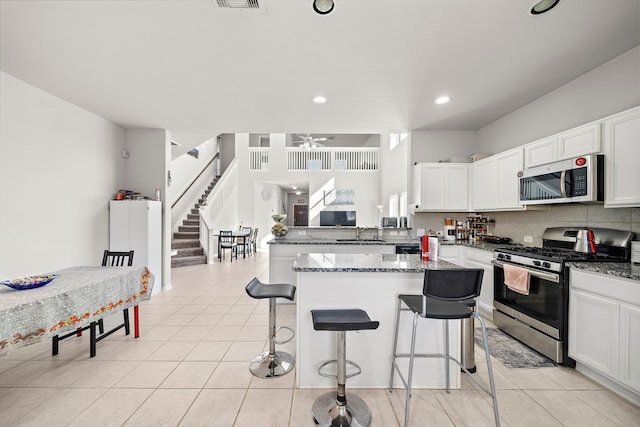 kitchen featuring a kitchen breakfast bar, stainless steel appliances, dark stone counters, sink, and white cabinets