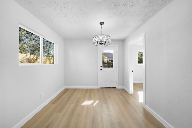 interior space with an inviting chandelier, light hardwood / wood-style flooring, a textured ceiling, and plenty of natural light