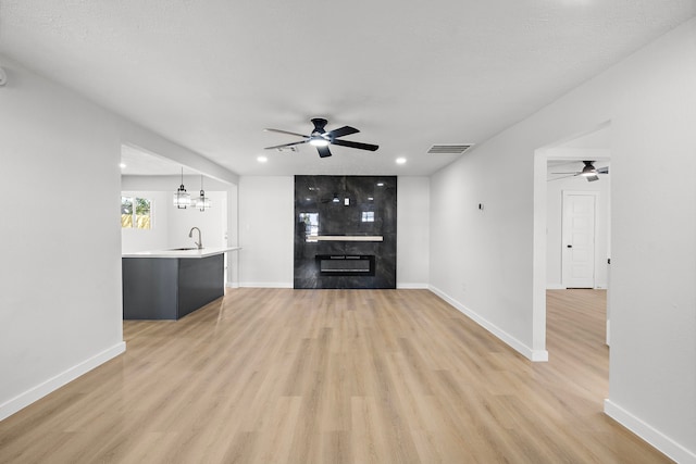 unfurnished living room with sink, a textured ceiling, light hardwood / wood-style flooring, and ceiling fan with notable chandelier