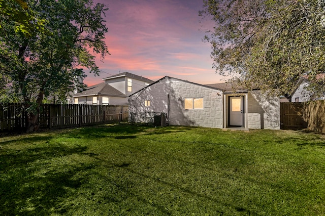 back house at dusk featuring a lawn