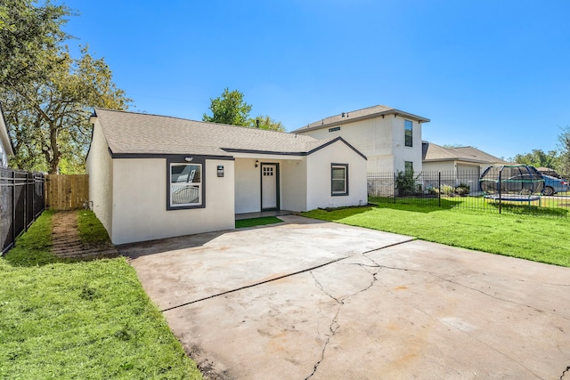 single story home featuring a front yard, a trampoline, and a patio