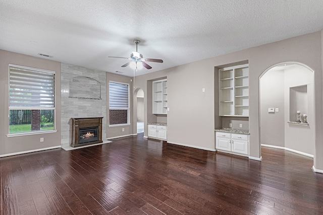 unfurnished living room featuring a large fireplace, dark hardwood / wood-style flooring, built in features, and a textured ceiling