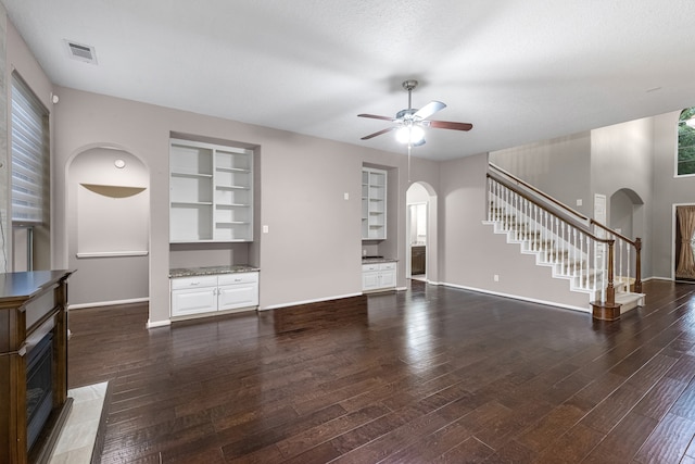 unfurnished living room featuring built in shelves, ceiling fan, dark hardwood / wood-style flooring, and a textured ceiling