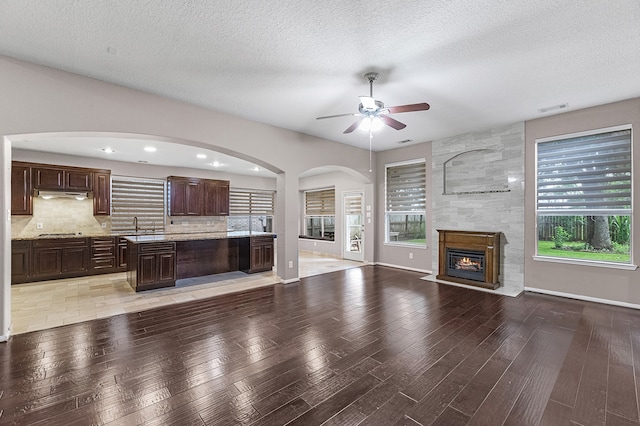 unfurnished living room featuring light wood-type flooring, a textured ceiling, a large fireplace, ceiling fan, and sink