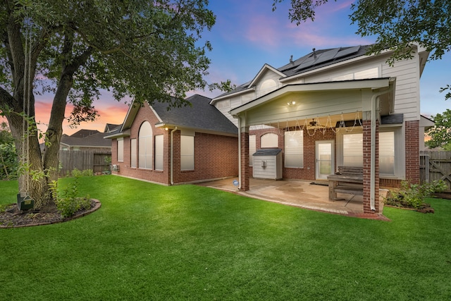 back house at dusk featuring a lawn, solar panels, ceiling fan, and a patio area