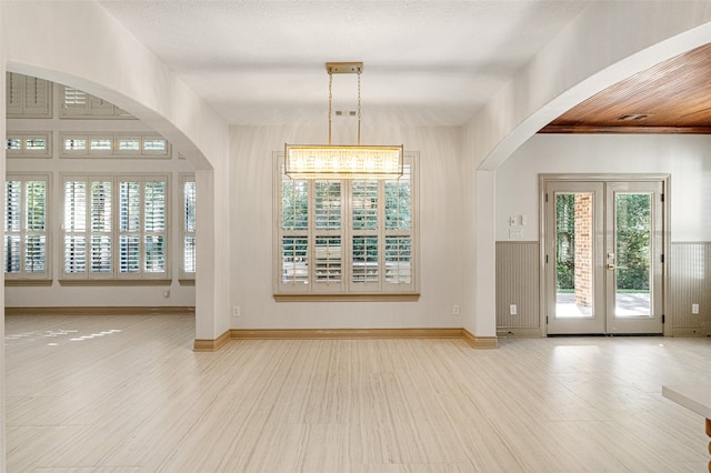 interior space with french doors, light wood-type flooring, a textured ceiling, and a notable chandelier