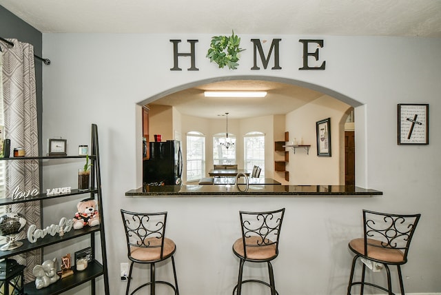 kitchen with decorative light fixtures, a chandelier, a breakfast bar area, and black refrigerator