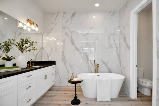 bathroom featuring hardwood / wood-style flooring, a tub, toilet, vanity, and tile walls