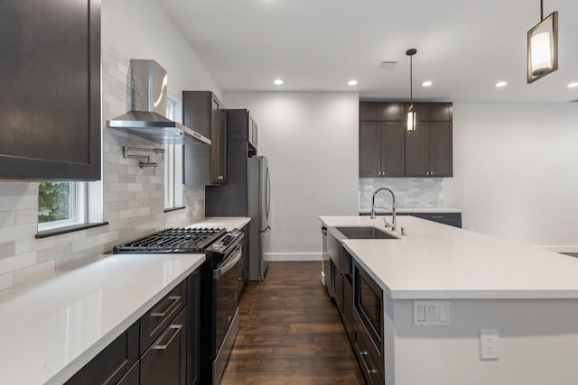 kitchen featuring dark hardwood / wood-style floors, wall chimney exhaust hood, hanging light fixtures, stainless steel appliances, and sink