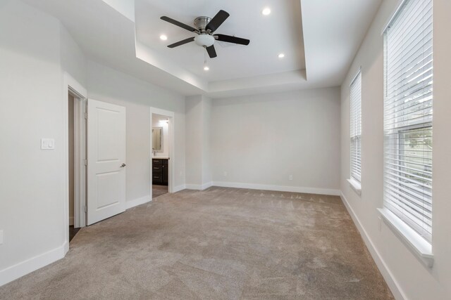 empty room with light carpet, ceiling fan, and a raised ceiling