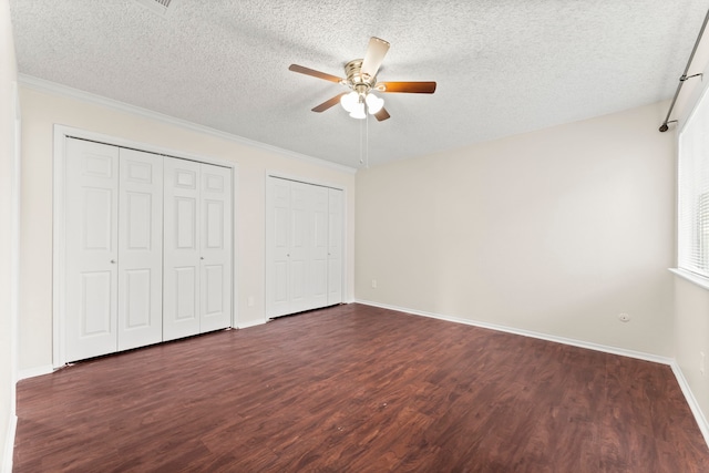 unfurnished bedroom featuring multiple closets, a textured ceiling, ceiling fan, ornamental molding, and dark hardwood / wood-style floors