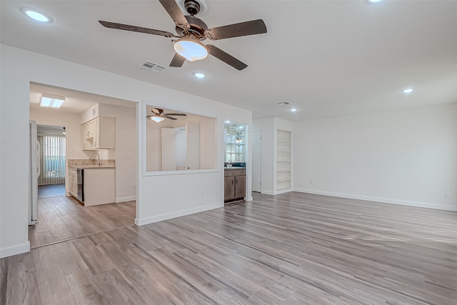 unfurnished living room with light hardwood / wood-style floors, sink, and ceiling fan