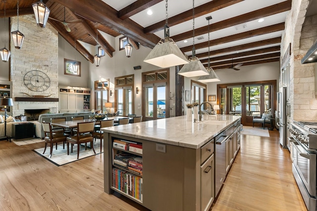 kitchen with sink, a center island with sink, beamed ceiling, stainless steel appliances, and light stone countertops