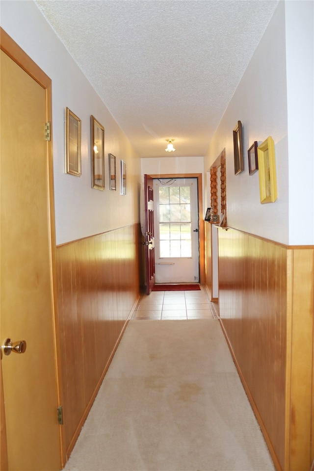 corridor with a textured ceiling, wooden walls, and light colored carpet