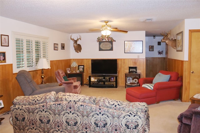 carpeted living room with ceiling fan, wood walls, and a textured ceiling