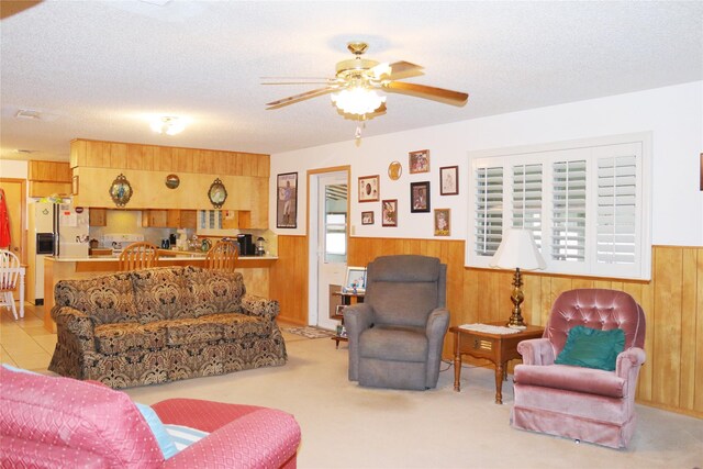 living room with ceiling fan, wood walls, a textured ceiling, and light colored carpet