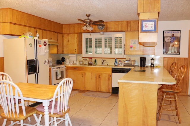 kitchen featuring a kitchen breakfast bar, a textured ceiling, sink, wooden walls, and white appliances