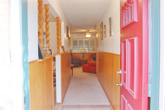 hallway featuring a wainscoted wall, a textured ceiling, carpet, and wooden walls