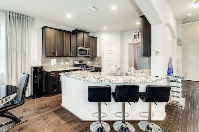 kitchen with tasteful backsplash, a breakfast bar area, appliances with stainless steel finishes, dark wood-type flooring, and light stone counters