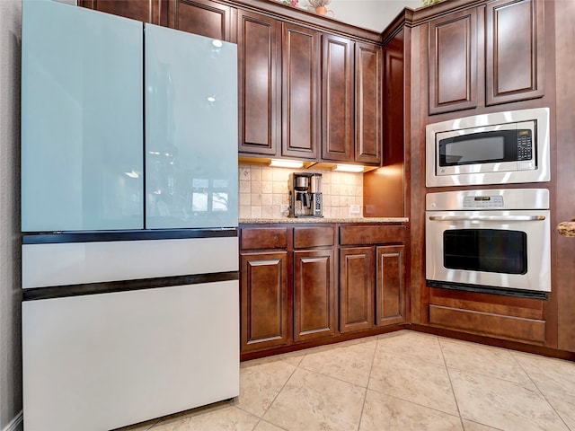 kitchen featuring stainless steel appliances, light stone counters, light tile patterned floors, and tasteful backsplash