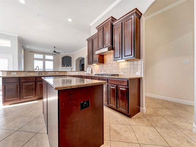 kitchen with kitchen peninsula, ceiling fan, light tile patterned floors, crown molding, and a center island