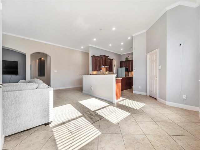 kitchen featuring light tile patterned floors, stainless steel refrigerator, a center island with sink, and crown molding