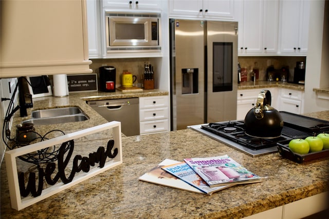 kitchen featuring appliances with stainless steel finishes, white cabinetry, light stone countertops, and sink