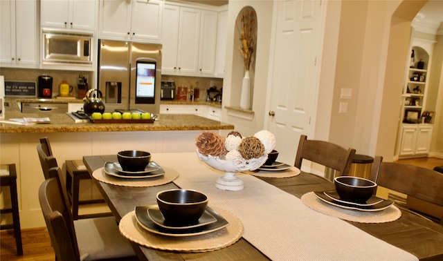 kitchen with appliances with stainless steel finishes, white cabinets, light stone counters, hardwood / wood-style flooring, and a breakfast bar