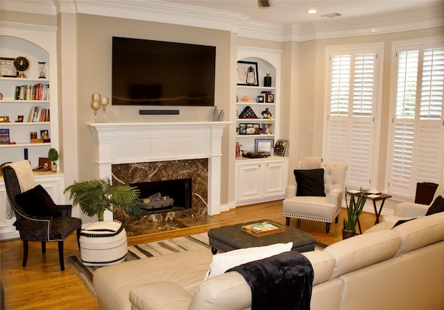 living room featuring a high end fireplace, built in shelves, ornamental molding, and light wood-type flooring