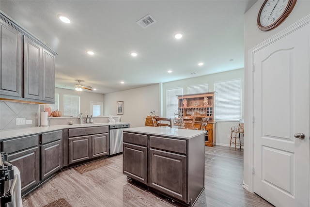 kitchen with tasteful backsplash, a kitchen island, stainless steel dishwasher, light wood-type flooring, and sink