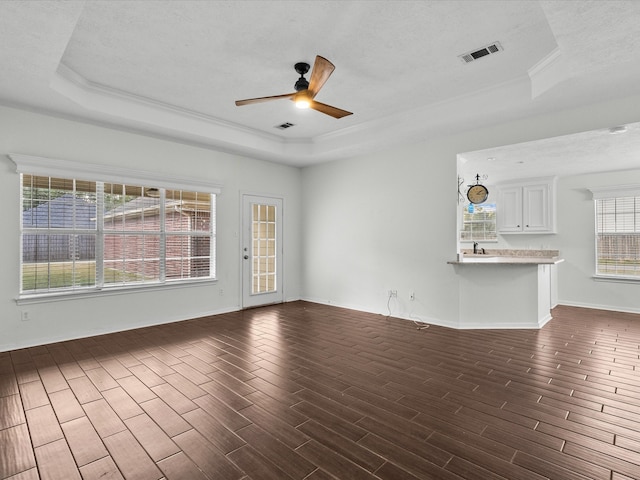 unfurnished living room with dark wood-type flooring, ceiling fan, a raised ceiling, and a textured ceiling