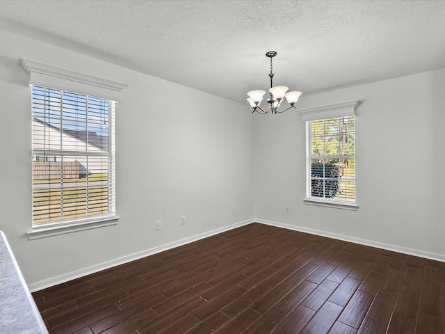 spare room with a textured ceiling, a chandelier, and dark hardwood / wood-style flooring