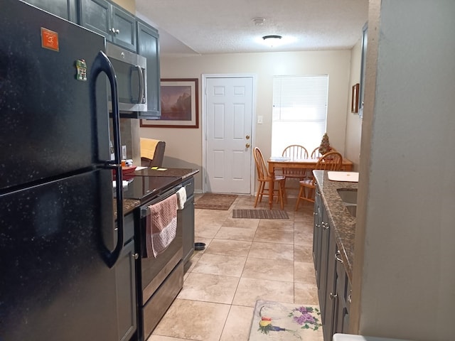 kitchen with appliances with stainless steel finishes, a textured ceiling, dark stone counters, and light tile patterned floors