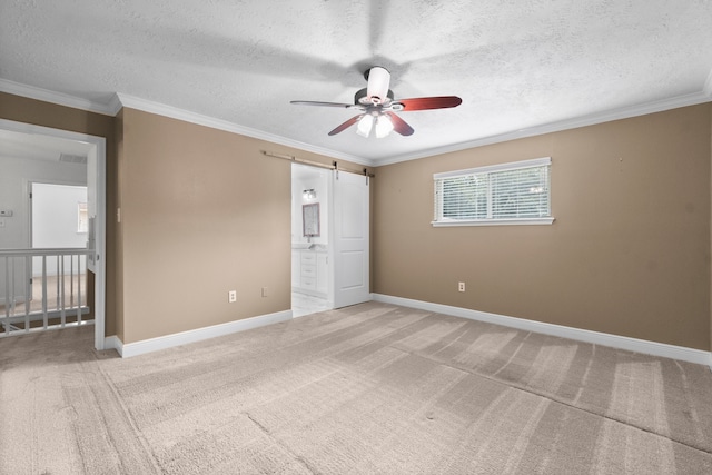 unfurnished bedroom featuring ensuite bath, a barn door, carpet flooring, a textured ceiling, and ceiling fan