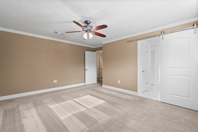 unfurnished bedroom with a barn door, a textured ceiling, ceiling fan, ornamental molding, and light colored carpet