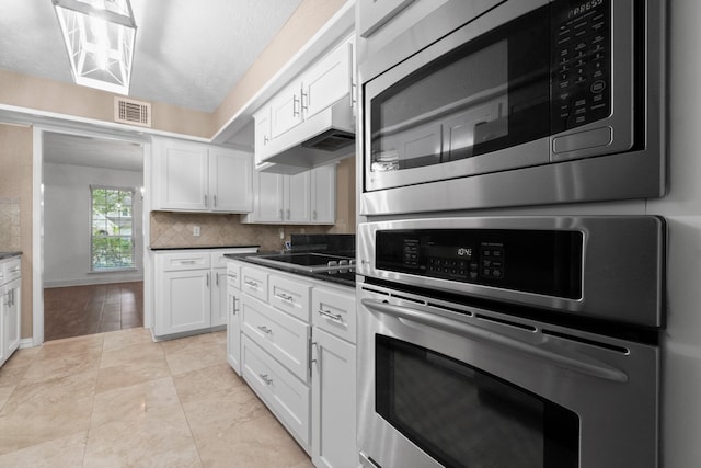 kitchen with backsplash, appliances with stainless steel finishes, a textured ceiling, white cabinetry, and light tile patterned flooring