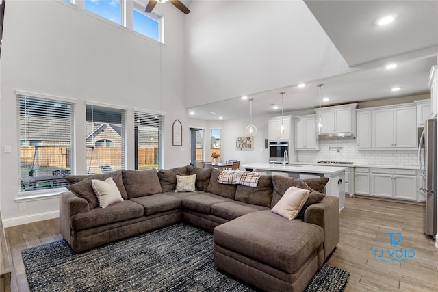 living room featuring a high ceiling, light wood-type flooring, and ceiling fan