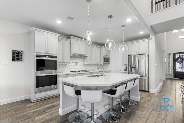 kitchen with dark wood-type flooring, appliances with stainless steel finishes, a kitchen island with sink, and white cabinets