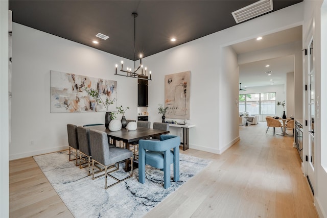 dining space with ceiling fan with notable chandelier and light hardwood / wood-style flooring