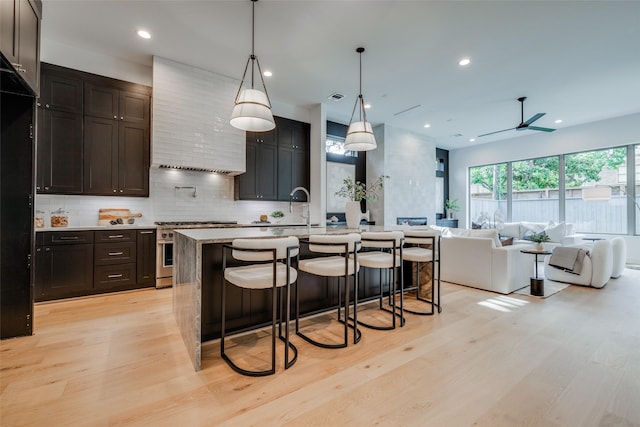 kitchen with light wood-type flooring, high end stainless steel range oven, and an island with sink