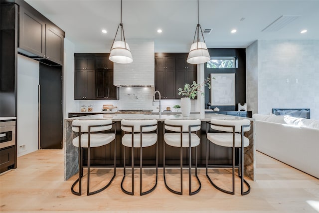 kitchen featuring pendant lighting, a center island with sink, a kitchen breakfast bar, dark brown cabinets, and light hardwood / wood-style floors